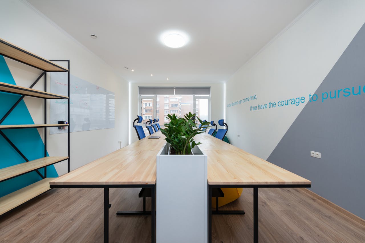 services-01 Wooden table with green plants placed in light conference room with empty shelves and motivational inscription on wall in office building